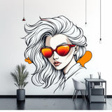 A modern wall decal featuring a stylized woman with white flowing hair and red-orange reflective sunglasses, in a bold comic book design above a monochrome cabinet in a contemporary room.