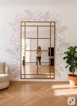 Vinyl wall decals of outline flowers and leaves arranged around a large rectangular mirror in a modern living room. The design is monochrome, cut from matte vinyl, and applied directly to the wall with no background.