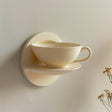 3D printed wall shelf shaped like a teacup and saucer, mounted on wall in soft natural light, modern minimalist kitchen or cafe decor accessory