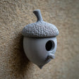 3D printed acorn-shaped birdhouse with round entrance and small cylindrical perch made of matte PLA plastic, mounted on a textured exterior wall.