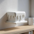 3D printed wall shelf shaped like a rectangular block with smooth dripping edges made of matte PLA plastic, mounted above a wooden shelf in soft natural daylight.