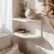 3D printed corner wall shelf in matte white PLA, mounted above a sofa with natural light and dried flowers, minimalist modern home decor accessory