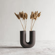 Dark U-shaped 3D printed vase with ribbed texture, styled with dried grasses for illustration; flowers are not included.