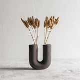 Dark U-shaped 3D printed vase with ribbed texture, styled with dried grasses for illustration; flowers are not included.