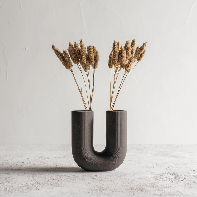Dark U-shaped 3D printed vase with ribbed texture, styled with dried grasses for illustration; flowers are not included.