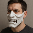 A man wearing a white 3D-printed half-face mask with a fierce, snarling expression and visible fangs, shown in a close-up angled view.
