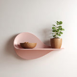 3D printed decorative wall shelf with abstract wavy shape in pastel pink, displaying a plant pot and wooden bowl as modern wall decor