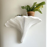 White 3D printed shelf shaped like a Turkey Tail mushroom, featuring gill-like grooves, mounted on a wall and styled with potted plants.