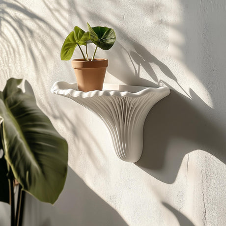 A sculptural white 3D printed wall shelf shaped like an Artist’s Conk mushroom, holding a small terracotta planter, mounted on a sunlit textured wall.