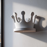 3D printed white crown-shaped wall shelf made from matte PLA, used as a small floating ledge on a light wall near a window.