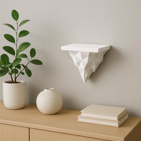 A white 3D printed wall shelf with a faceted, geometric triangle base mounted on a light gray wall above a modern wood sideboard with minimalist decor.