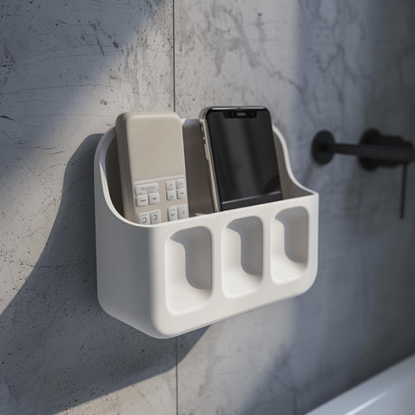 3D printed white wall-mounted organizer shelf with two upper compartments for phone and remote and three small front pockets, installed above a bathroom sink on a textured grey wall.