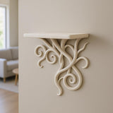 A sculptural 3D printed wall shelf with intricate curling vine-like supports in a light matte finish. The shelf is mounted on a neutral wall in a softly lit living space, offering an artistic and organic visual accent.