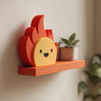 3D printed wall shelf with a flat ledge and attached smiling flame character made of matte PLA plastic, mounted on an interior wall near plants.