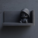 3D printed matte PLA wall shelf with a small hooded figure sitting in the back corner of a rectangular ledge on a dark textured wall.