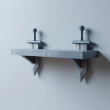 3D printed matte PLA wall shelf with two stylized sword-shaped supports mounted on a light-colored wall.