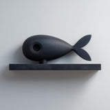 3D printed matte PLA wall shelf with a stylized fish figure resting on a slim rectangular ledge, mounted on a light-colored wall.