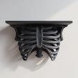 3D printed matte black PLA wall shelf with a realistic ribcage and spine forming the support under a flat rectangular ledge.