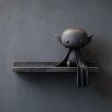 3D printed matte PLA wall shelf with a small vampire bat character and cape sitting on a double-step ledge against a dark wall.