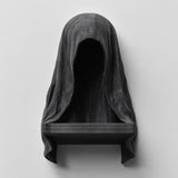 3D printed matte black wall shelf shaped like a hooded cloaked figure with a dark empty face and a small ledge at the bottom, mounted on a light wall.