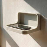 3D printed wall-mounted phone shelf with a minimalist floating design holding a smartphone, mounted near a window with soft natural light.