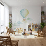 A soft watercolor illustration of a single hot air balloon in light blue and pale yellow, floating above several whimsical, swirling light green and blue clouds on a plain white background.