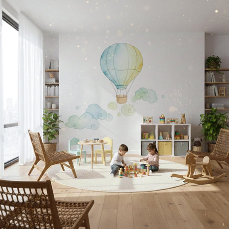 A soft watercolor illustration of a single hot air balloon in light blue and pale yellow, floating above several whimsical, swirling light green and blue clouds on a plain white background.