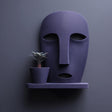 3D printed wall mounted face-shaped planter shelf with a small plant pot, displayed against a dark minimalist wall with soft directional lighting.