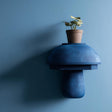 3D printed modern mushroom wall shelf with rounded dome cap and smooth sculptural base, mounted on a blue minimalist interior wall.