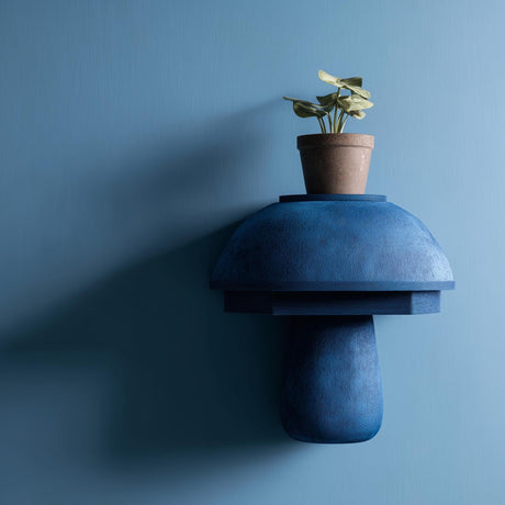 3D printed modern mushroom wall shelf with rounded dome cap and smooth sculptural base, mounted on a blue minimalist interior wall.