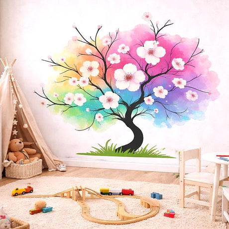 A watercolor illustration of a black tree silhouette with small white flowers. The leaves of the tree are represented by a large, soft-edged cloud of vibrant rainbow colors including pink, purple, blue, green, and yellow. The tree is growing from a small patch of green grass on a white background.