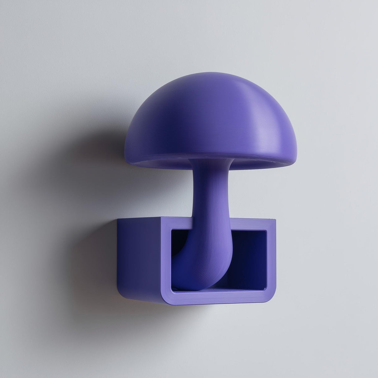 3D printed mushroom wall shelf with a domed cap and stem flowing into a small rectangular cubby tray, visible print texture, mounted on a clean wall.