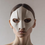 3D printed geometric face mask with sharp folded facets and almond eye openings, minimalist half-mask style, worn in a studio portrait on a neutral background.