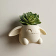 3D printed kawaii bunny wall planter in matte cream PLA mounted on a neutral wall, holding a small green succulent plant.