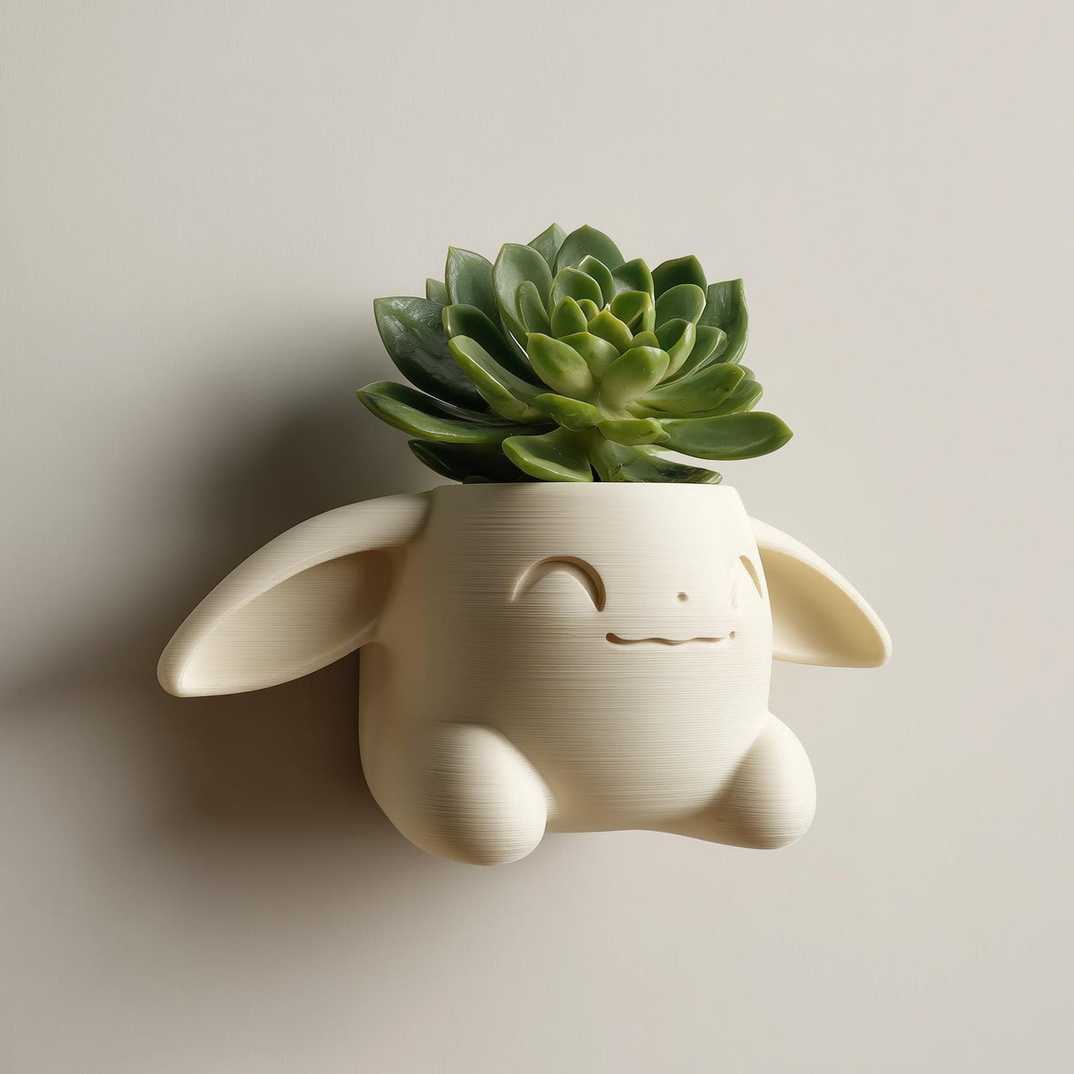 3D printed kawaii bunny wall planter in matte cream PLA mounted on a neutral wall, holding a small green succulent plant.