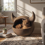 Horned floor cat cave bed with a rounded enclosed pod shape and two curved horn accents, textured surface, with a cat resting inside in a cozy living room.