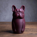 3D printed French bulldog-shaped pet ashes urn with a fitted lid seam at the neck, visible print texture, on a wooden tabletop with a neutral studio backdrop.
