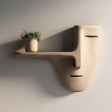 3D printed wall mounted shelf shaped like a minimalist face mask with a long nose-style floating ledge, holding a small potted plant on a plain wall.