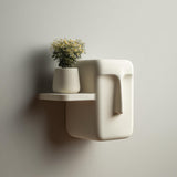 3D printed minimalist face-inspired wall shelf with a compact floating ledge and sculptural side detail, holding a small vase, mounted on a clean wall in soft light.