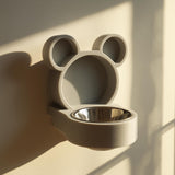 3D printed bear-shaped wall mounted pet bowl holder with round ears and a circular bowl opening, photographed in warm sunlight on a clean wall.