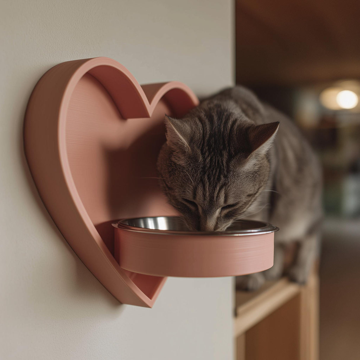 3D printed heart-shaped wall mounted pet bowl holder with a round bowl opening, shown with a cat eating from a metal bowl in a cozy home interior.