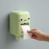 3D printed kawaii monster wall mounted toilet paper holder with round eyes and small teeth, dispensing toilet paper from the mouth opening, hand pulling sheet.