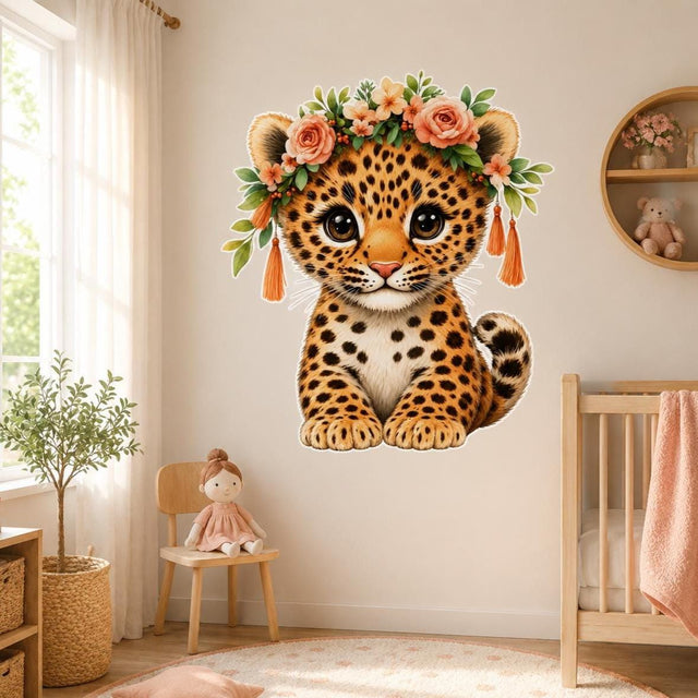 Front-facing contour-cut sticker of a seated baby leopard with large brown eyes, orange-and-black spotted fur, and a cream chest. The cub wears peach roses, coral flowers, green leaves, berries, and orange tassels. The design has no background and features a slim white outline around its shape.