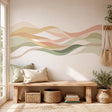 Abstract horizontal design made of overlapping flowing wave shapes in sage green, olive, beige, cream, sand, and muted terracotta tones on a white background.