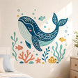 Stylized dark teal whale with a peaceful closed eye and decorative floral patterns, surrounded by three small fish, bubbles, coral, seaweed, a starfish, stones, and yellow sea sponges in teal, mint, coral, and mustard tones.