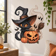 Black cat in a pointed witch hat behind a grinning pumpkin, with a smaller pumpkin, broom, bats and cream swirls.