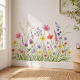 Watercolor meadow of delicate wildflowers in pink, coral, yellow, lavender, violet, and soft blue, growing among tall grasses, slender stems, and layered green foliage.