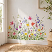 Watercolor meadow of delicate wildflowers in pink, coral, yellow, lavender, violet, and soft blue, growing among tall grasses, slender stems, and layered green foliage.