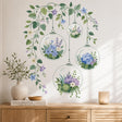 Four transparent hanging terrarium globes filled with blue, lavender, cream, and white flowers, succulents, and greenery, suspended beneath cascading leafy vines with delicate blossoms and buds.