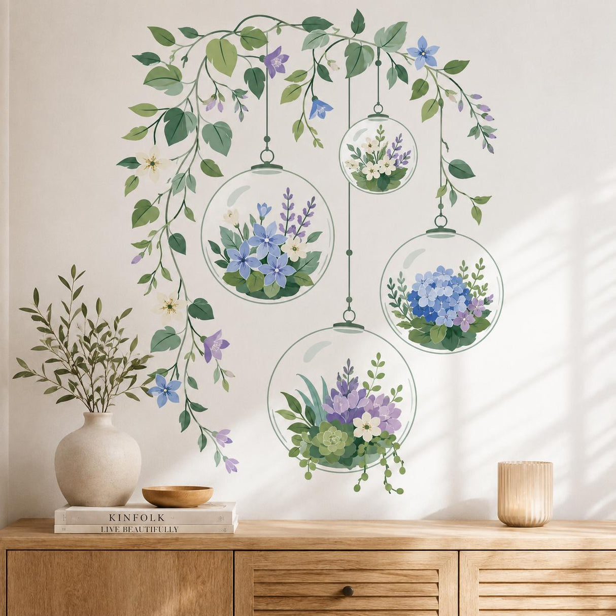 Four transparent hanging terrarium globes filled with blue, lavender, cream, and white flowers, succulents, and greenery, suspended beneath cascading leafy vines with delicate blossoms and buds.